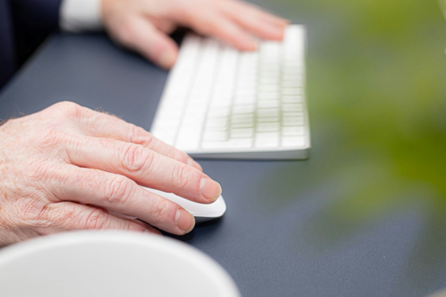 Close-up of a hand using a computer mouse beside a white keyboard
