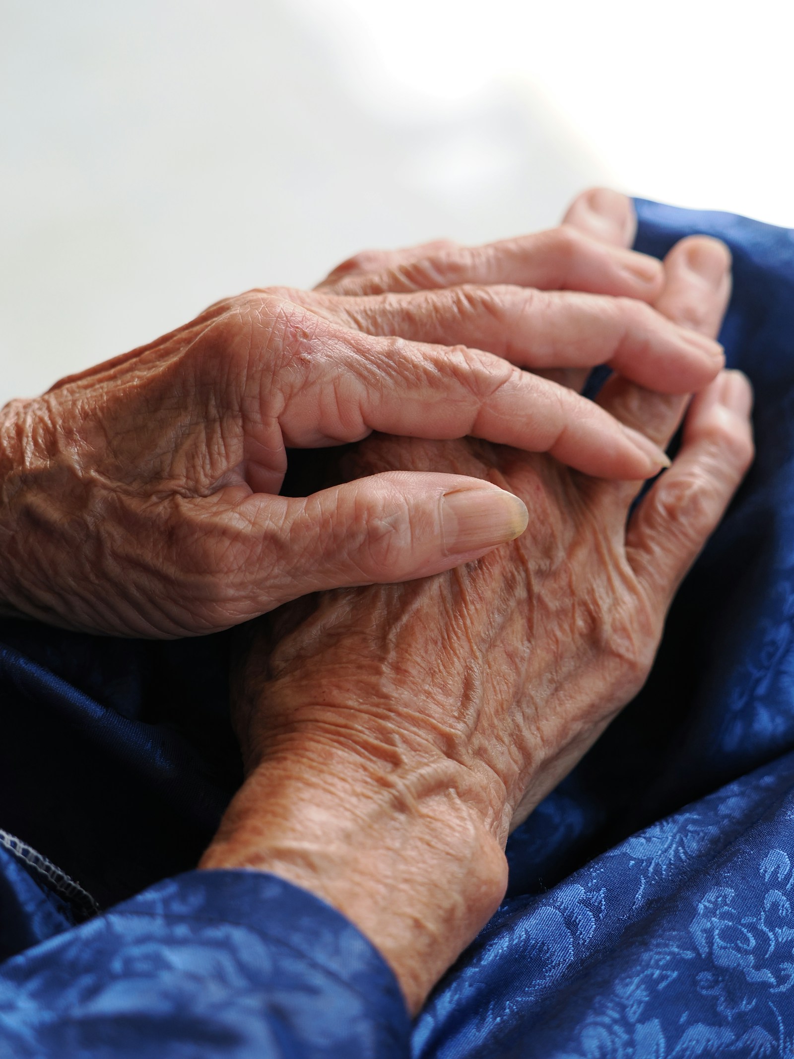 Close-up of an older person’s hands resting together on blue fabric