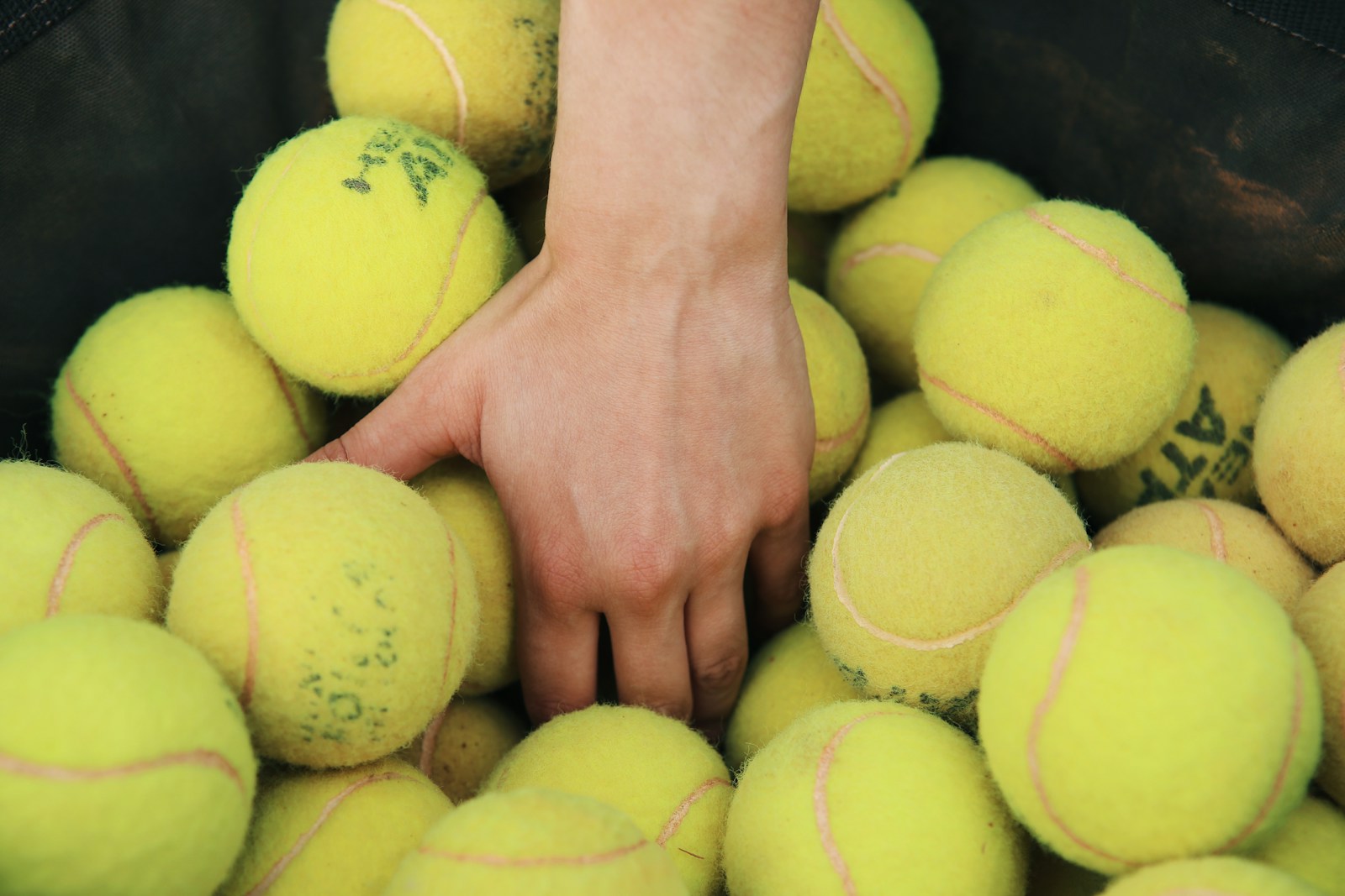 One hand reaching among tennis balls, showing natural wrist and finger positioning